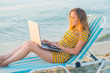 Fit young woman sitting on deck chair at sea view beach using laptop. Female freelance programmer...