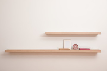 Wooden shelves with books, photo frame and clock on light wall
