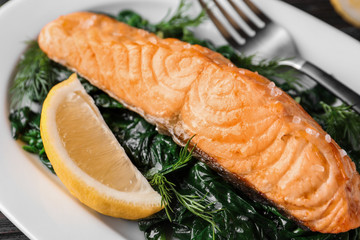 Tasty salmon with spinach and lemon on plate, closeup