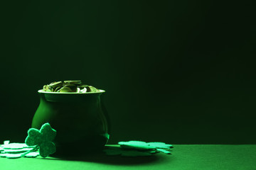 Pot of gold coins and clover leaves on green table against dark background, space for text. St....