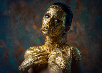 Girl with a mask on her face made of gold leaf. Gloomy studio portrait of a brunette on an abstract background.
