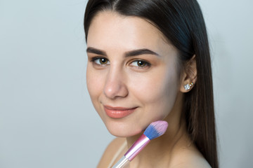 Close-up of a young girl in a light top on a white background making a facial make-up. A pretty...