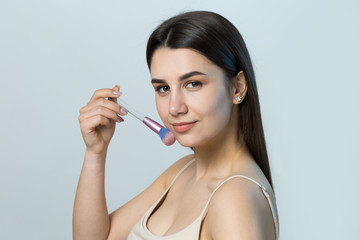 Close-up of a young girl in a light top on a white background making a facial make-up. A pretty woman holds a cosmetic brush near her face and smiles.