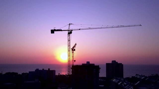 Silhouette of a crane in action at a construction site and stunning sunset in the background.
