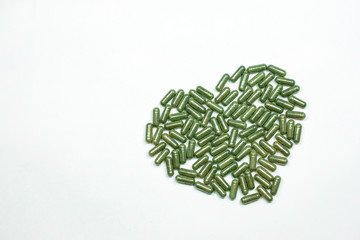 Green Herbal capsules pills in hart shape from herbs on white background, pills top view..