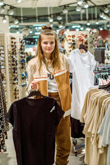 Shopping concept .teenager girl tries on and buys a sports shirt in the mall. The choice is white or black. A large selection of clothes in the store, black Friday sales. Showcase with sunglasses