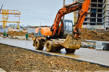Big bright yellow powerful industrial heavy excavator tractor, bulldozer, specialized construction equipment for road repair during the construction of a new micro-district in a big city