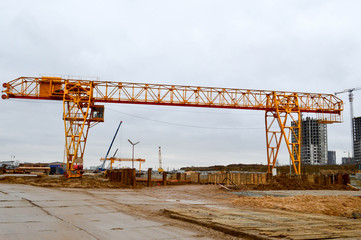 Fototapeta na wymiar High heavy yellow metal iron load-bearing construction stationary industrial powerful gantry crane of bridge type on supports for lifting cargo on a modern construction site of buildings and houses