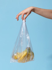 A woman's hand holds a bunch of ripe bananas in a plastic bag