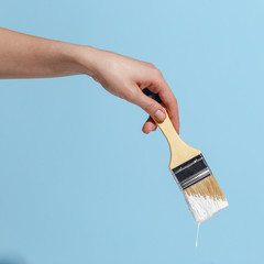 A woman's hand holds a brush with white paint