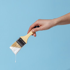 A woman's hand holds a brush with white paint