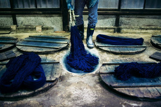 Close up of man beating indigo dye into strands of cotton.