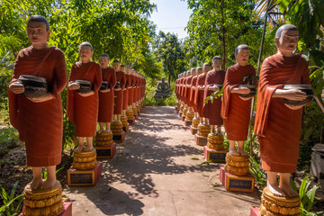 Row of Buddhist monk statues with red robes and alms bowls in the gardens of the Buddhist Temple at Siem Reap,Siem Reap