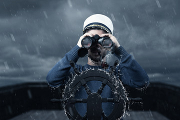helmsman with binoculars and cap viewing the coast and light tower in depth of field - obrazy, fototapety, plakaty