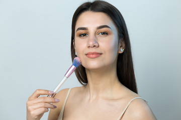 Close-up of a young girl in a light top on a white background making a facial make-up. A pretty...
