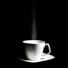 A low key photography of a white cup on top of a saucer, getting sugar poured into it in front of a complete black background