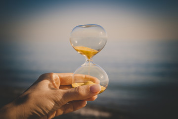 Sand in the hourglass and sand on the sea, time in the hands of a young girl, the concept of falling grains of sand in a glass flask