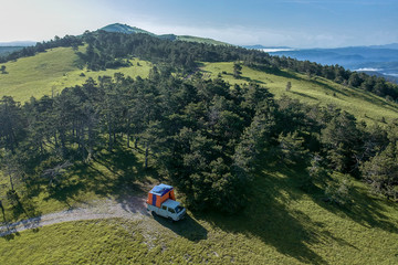 Aerial photo of a van with a tent on the back on the top of the mountain. Off grid camping in wild forests, away from civilisation, modern nomad.