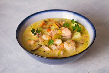 Bowl of seafood chowder with salmon on white background