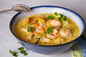 Bowl of seafood chowder with salmon on white background