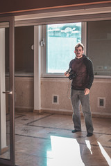 Man standing in an apartment next to a window holding a vintage photo camera in his hand. Copyspace on left.