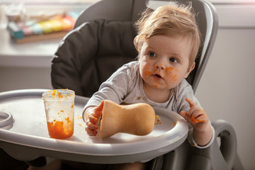 Beautiful baby in the child dining chair eat healthy, vegetable food. Child eat  pumpkin and carrot...