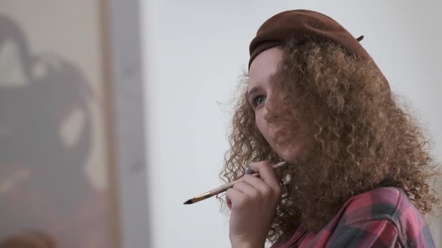 Curly girl dreamy holds a brush , looks at her painting work and then does a few dabs