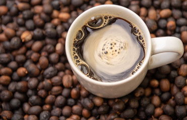 cup of coffee with cream and roasted coffee beans scattered around it