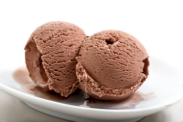 two frozen balls of chocolate ice cream on porcelain saucer close-up against white background 