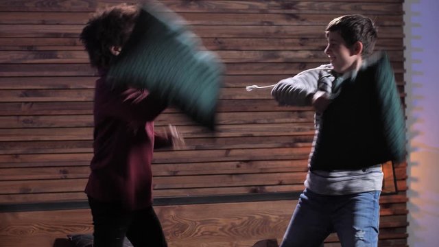 Joyful mixed race teenage boys having fun at home while beating with pillows. Active diverse teenagers spending domestic leisure fighting pillows on bed jokingly declaring war on each other