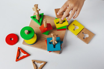 Child plays  Montessori toy. Multicolored logic sorter on white background. Baby Hands close-up. Wooden geometric shapes circle, square, triangle, rectangle.  View from above