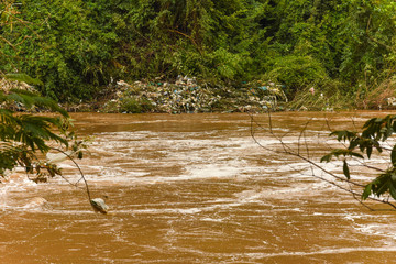 garbage washed ashore in filthy overflowing river