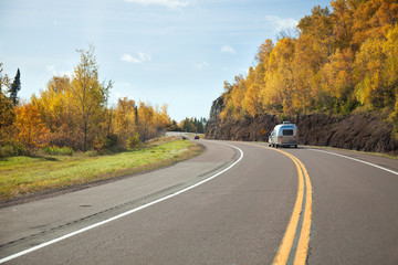 Truck and camping trailer drive along curving road on the north shore of Lake Superior in northern...