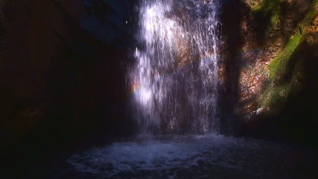 Rainbow reflecting through waterfall flowing over moss covered rocks 