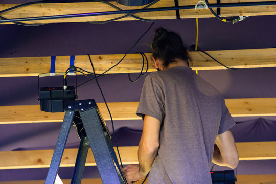 A lose up and rear view of a man at work backstage during a multicultural festival, stagehand working from ladders preparing equipment for music set