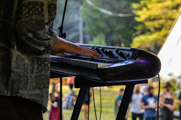 Close up view of an electronic keyboard player during an EDM music set at a cultural earth dance festival for peace, with blurry people in background