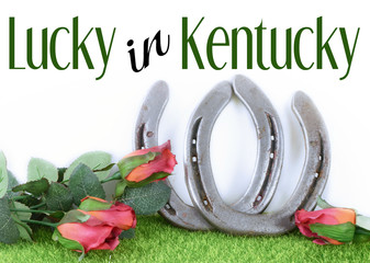 Kentucky derby image of a pair of horseshoes and red roses on green grass with white background....
