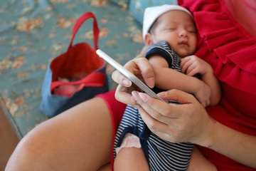 mother using mobile phone technology and a little baby sleeping