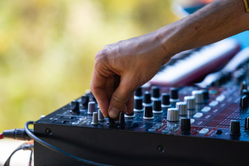 A close up selective focus shot on the hand of an electronic dance music DJ using mixing equipment on stage. during day at earth and culture festival