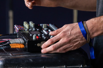 A close up and side view on the hands of a man operating an electronic music mixer during a set. at a festival celebrating acoustic beats and earth