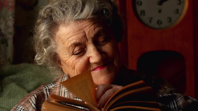Elderly woman reading old book on a dark background