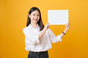 Fototapeta na wymiar Young Asian woman holding blank paper with smiling face and looking on the yellow background. for advertising signs.