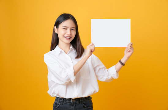 Young Asian woman holding blank paper with smiling face and looking on the yellow background. for advertising signs.