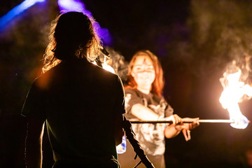 A selective focus shot of fire performers using a burning lance by night at a festival celebrating artisans, earth and alternative communities