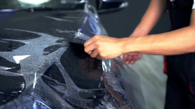 Car wrapping specialists straightening protective film  putting vinyl foil or film on black car.