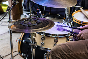 Fototapeta na wymiar A close up view of a drum kit and the legs and hands of a drummer playing on stage. during a folk music set at an alternative communities festival