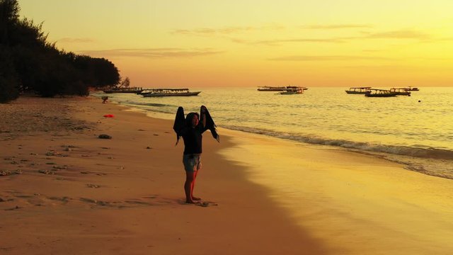 Silhouette of girl with towel on calm exotic beach watching beautiful sunset with yellow sky reflecting on sea surface, Myanmar