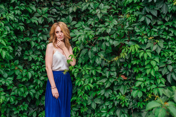 Fototapeta premium Portrait of a young beautiful woman, standing next to the wall of wild grape leaves.