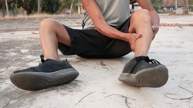Asian senior man sitting and touching painful leg cramp while workout in the park. Healthy lifestyle and Healthcare concept.