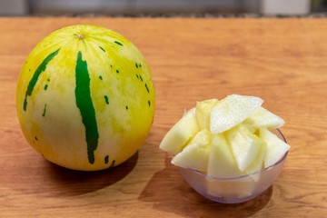 Yellow melon in pieces served in a bowl and in the background the whole fruit